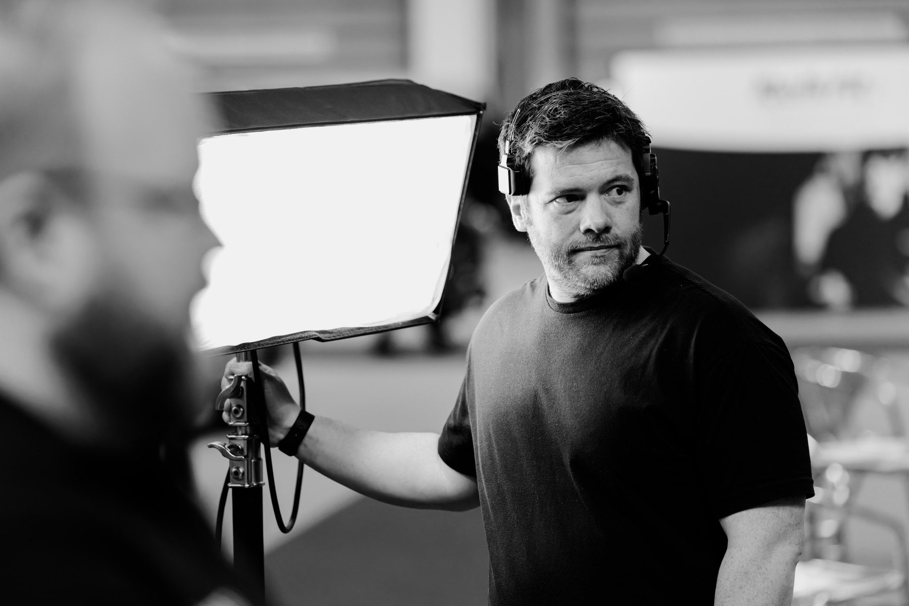 Thom on set in a headset, one hand steadying a lit softbox on its stand