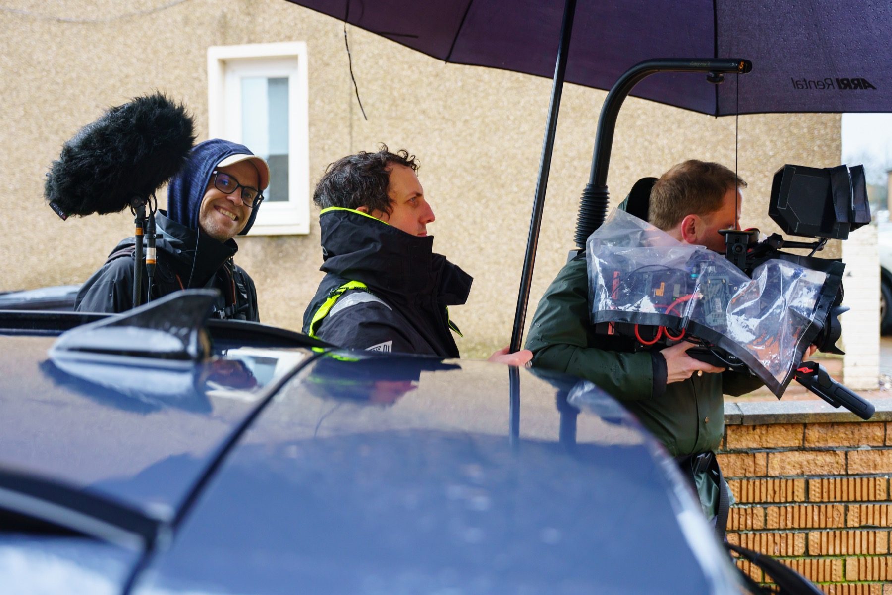 Three of the IRIS crew filming on a street in the rain, boom mic up and the camera under a rain cover