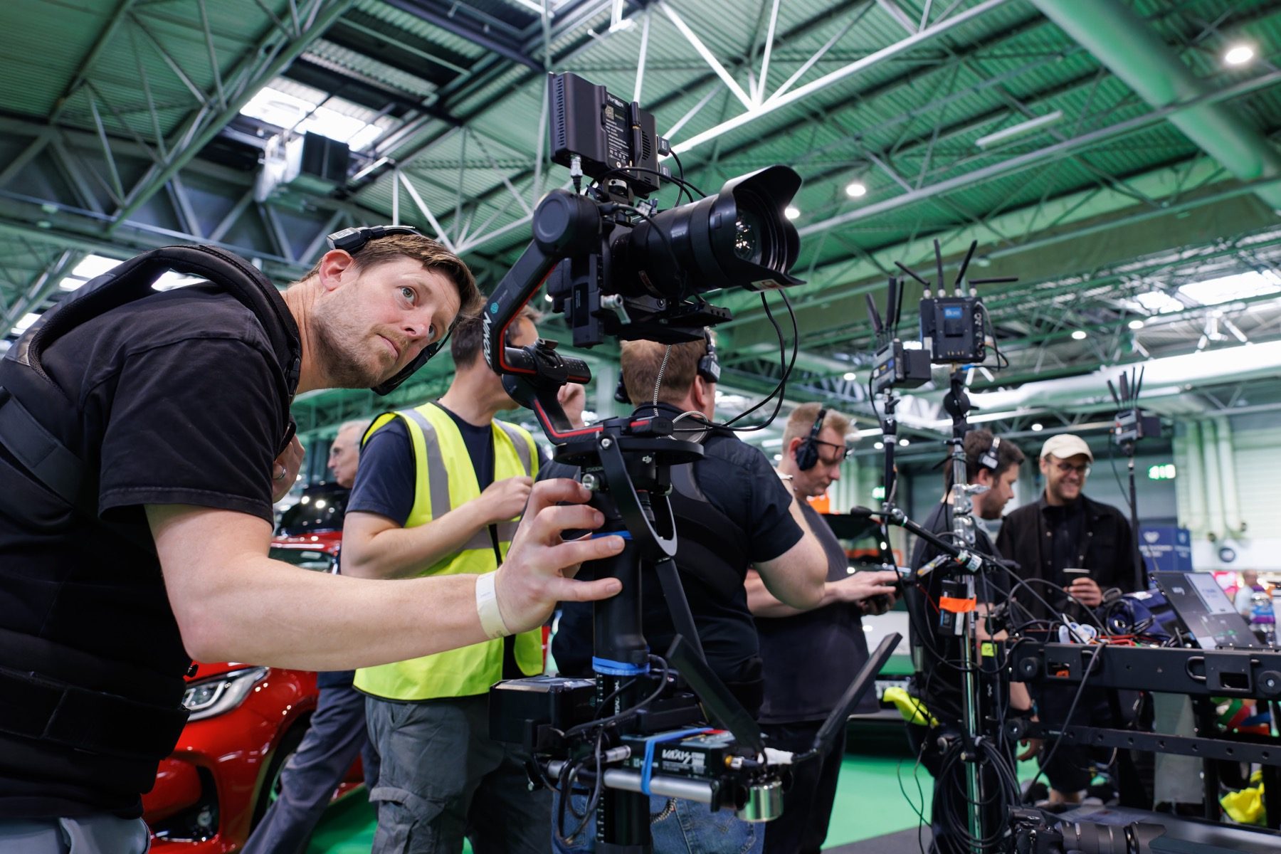 An IRIS operator in a support vest balancing a gimbal rig on the floor of a live event, camera crew working behind