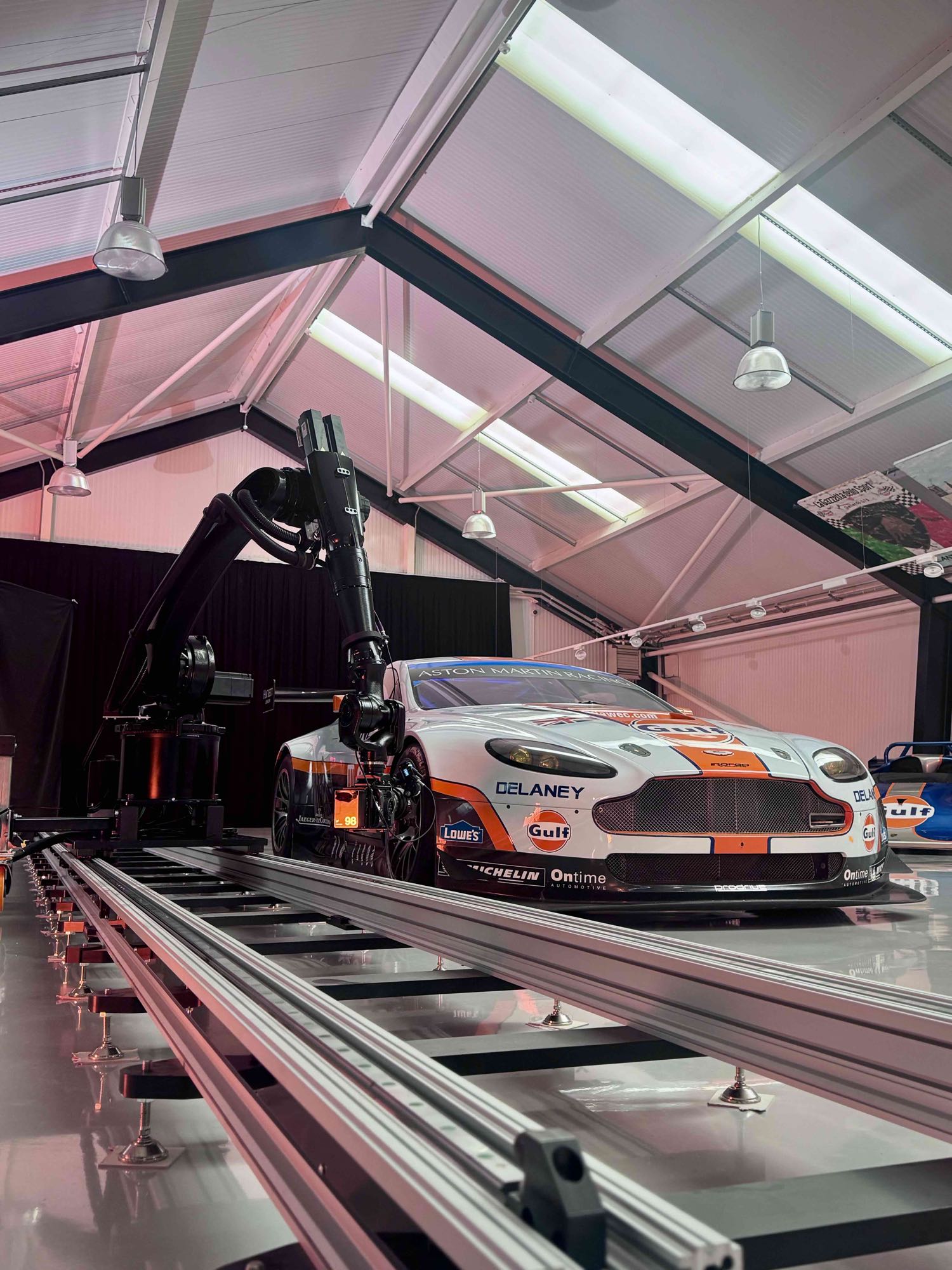 The IRIS robot arm and camera on its track, running alongside a Gulf-liveried Aston Martin Racing GTE under the collection's skylights