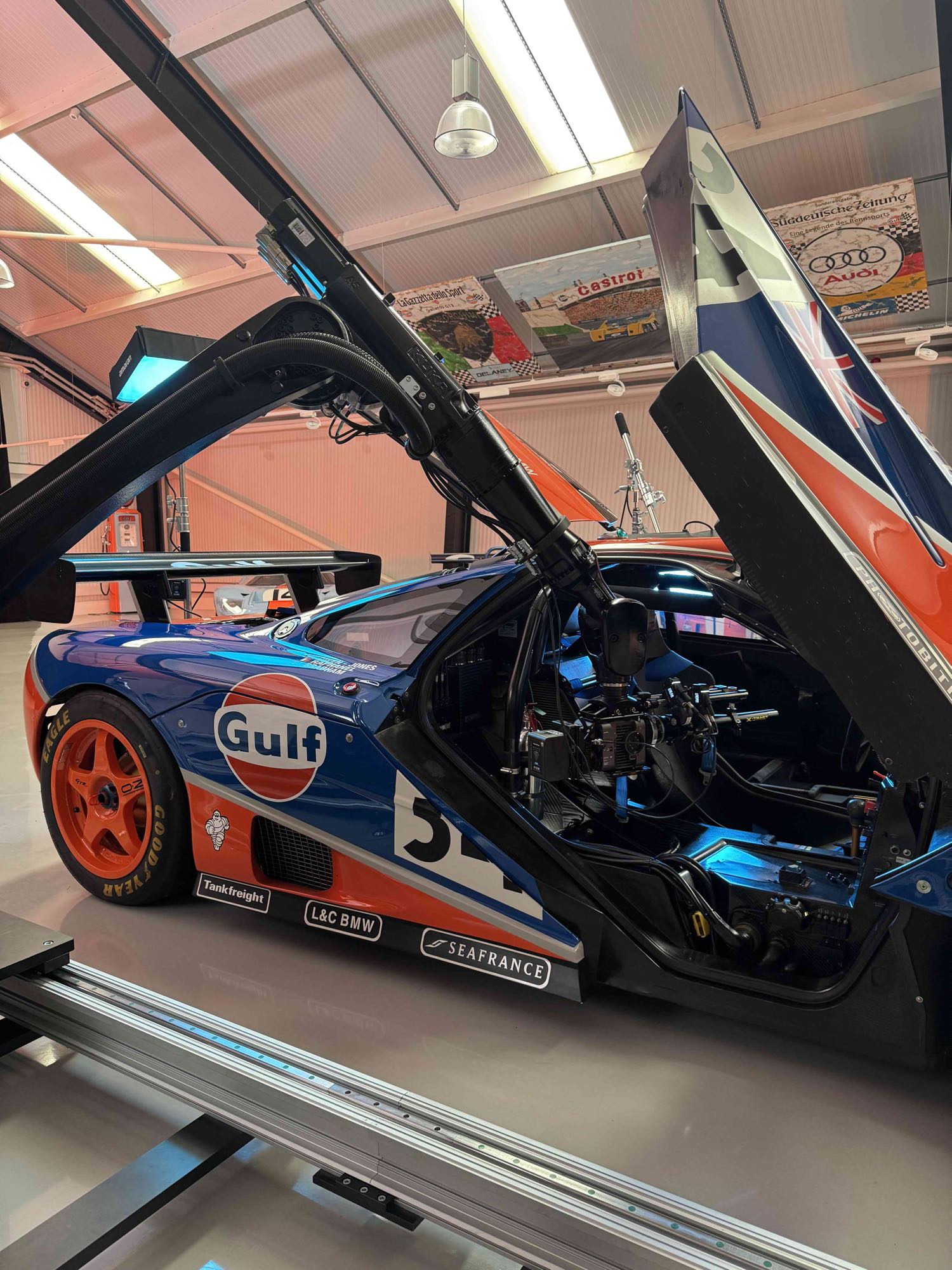 The IRIS robot arm reaching in over the open dihedral door of a Gulf-liveried McLaren F1 GTR, camera positioned across the cockpit