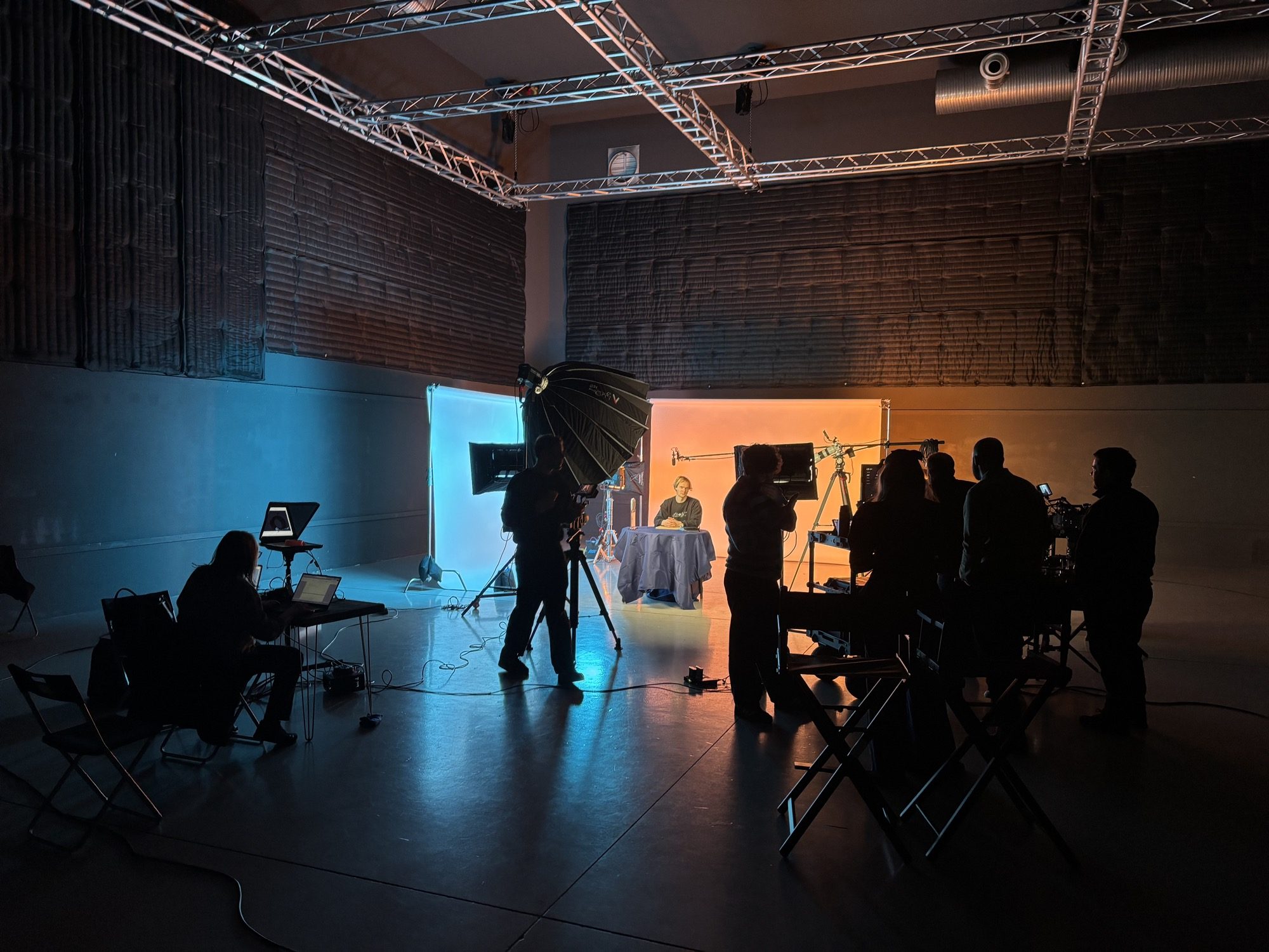 The full IRIS crew around a gelled interview set on the driver shoot: softboxes, monitors and camera in silhouette, the talent lit at the far end